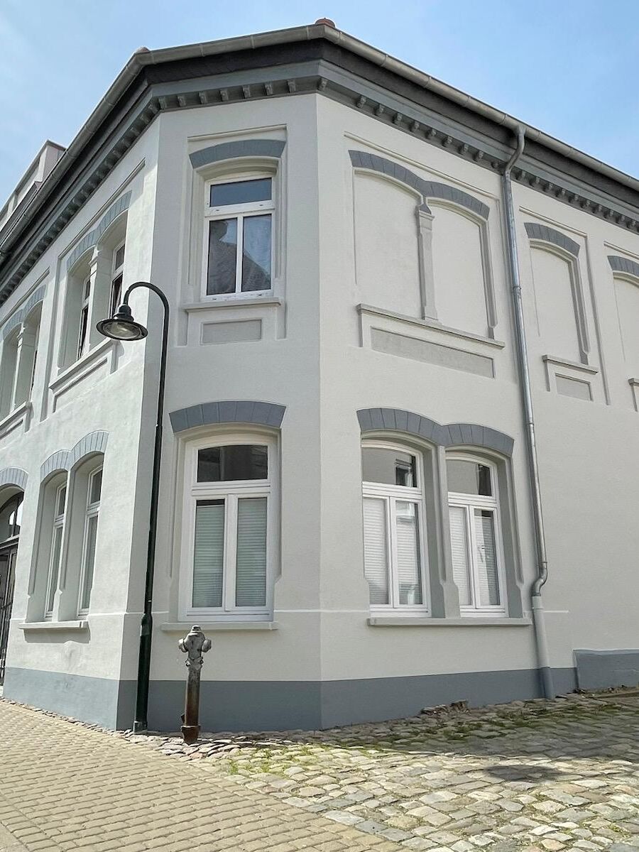 Nachher: frisch sanierte Altbaufassade mit hellem Anstrich und grauen Zierelementen